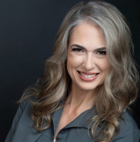 Rachael lundin Author photo. She has long brown hair turning silver, a grey button up shirt, and a big smile.